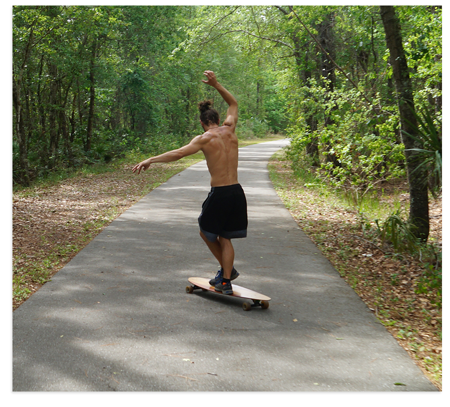 dancing on a longboard on paved path through woods