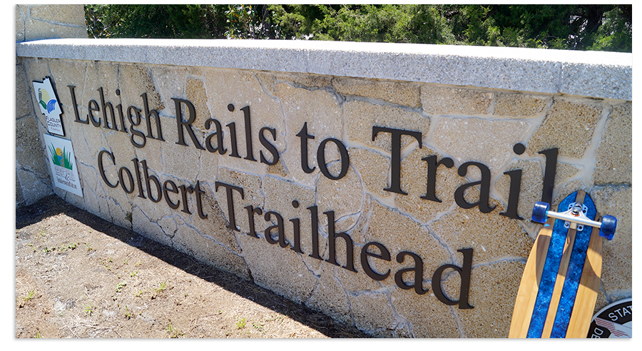 blue classic stripe longboard posing with lehigh rails to trails sign